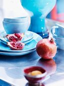 Pomegranates and pastel blue china crockery on shiny table top