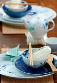 An Asian place setting - chopsticks and rice noodles in a bowl in front of a small teapot