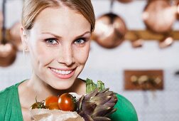 A young woman holding a paper bag of fresh vegetables