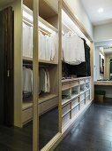 Open cupboard with clothing hung on rods in a dressing room