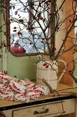 Branches of rosehips with fairy lights in china jug on vintage table below window