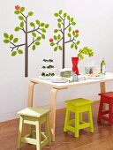 Dining table and colourful stools in front of tree-motif wall stickers