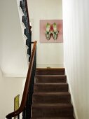 View up staircase with brown carpet and wrought iron balustrade to picture with shoe motif on wall of traditional staircase