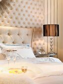 Sektgläser auf Doppelbett vor gepolsterter Wandverkleidung und Nachttisch mit grossem, geschliffenem Bergkristall