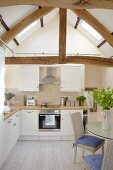 Bright kitchen with white cupboards and dining area below gable beams
