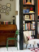 Green metal chair in front of antique bureau next to open doorway with view of white chair in front of bookcase
