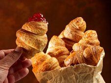 Croissants in a paper bag and one in a hand with redcurrant jam