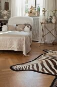 Chaise longue next to side table and zebra-skin rug on parquet floor in bedroom