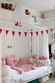 White canopied bed with pink scatter cushions and blanket in girl's bedroom