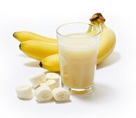 A glass of banana juice with bananas in the background and banana slices next to it