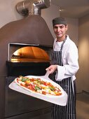Pizza chef holding pizza in front of oven