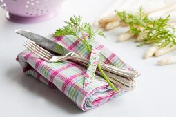 A place setting with carrot leaves, white asparagus in the background