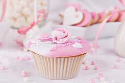 A cupcake with pink and white glaze, sugar roses and sugar pearls