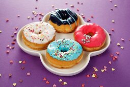 Four doughnuts with colourful glaze and sugar sprinkles