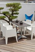 Modern dining set made from bistro tables and white chairs next to a small tree on a wooden terrace