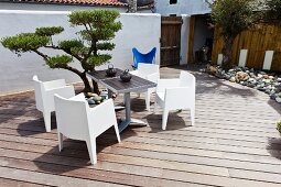 Two bistro tables and modern, white garden chairs next to a small topiary tree on a terrace