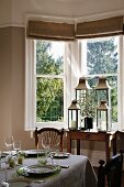 Set table and collection of lanterns in dining room with bay window