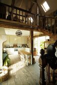 Open-plan, country-house-style living-dining room with rustic wooden floor and wooden staircase leading to mezzanine