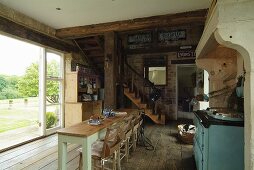 Open-plan, country-house-style living-dining room with rustic wooden floor and wooden staircase leading to mezzanine; open terrace window leading to garden