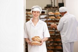 Bäckerin mit Brotlaiben, im Hintergrund Bäcker vor Brotregal