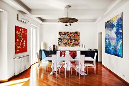 Expressionist paintings provide a visual backdrop for a modern dining table with designer chairs
