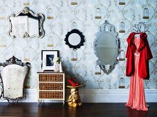 Collection of antique mirrors on patterned wallpaper as a background for red pumps on a table made from a garden gnome painted gold and red evening dress on a clothes hanger on a clothes stand