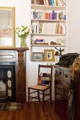 Patchwork cushion on antique wooden chair between chest of drawers and open fireplace in corner of room with dresser built into niche