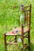 Flaschen mit Wiesenblumen hängen am Holzstuhl