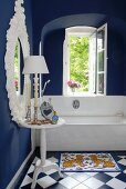 Traditional bathroom in blue and white - white tiled bathtub below open window with view of garden in dark blue painted bathroom