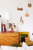 Retro Sideboard mit japanischen Puppen und Schirmlampe neben Stuhl und Handtaschen an der Wand