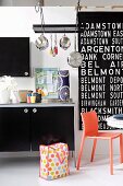 Young, hip kitchen design with large, black and white lettering on the wall, hanging pots and bright orange plastic chair