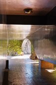 Tunnel-like entrance walkway composed of dark polished curved walls raised on square tiled plinths