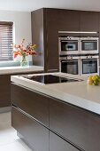 Kitchen island and fitted appliances in designer kitchen with brown cupboard doors