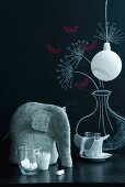 Filzelefant mit Gläsern und minimalistische Hängeleuchte vor floral gestalteter Tafelwand