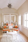 Orientalisches, helles Schlafzimmer mit weißem Beistelltischchen und gedecktem Tablett; filigrane Metallstühle mit orange-beigen Polstern laden zur Teezeremonie ein