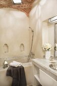 Corner of Oriental bathroom with vaulted brick ceiling and tealights in small arched niches; bathtub and washstand clad in pale stone slabs