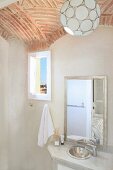 Spherical pendant lamp hanging from vaulted brick ceiling above simple washstand with mirror in Oriental bathroom; view through small window