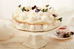 Geschichtete Baisertorte mit essbaren Blumen auf einem weißen Tortenständer