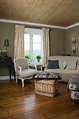 Pleasant living room with vintage furniture upholstered in natural colours and large wicker trunk as coffee table