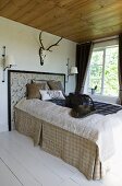 Stately bed with rustic bedspread in natural fibres below stag antlers