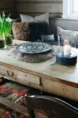 Candle lantern and ethnic bowl on rustic wooden coffee table in front of sofa with fur scatter cushions