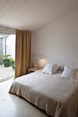 Simple living room with double bed next to floor-to-ceiling windows