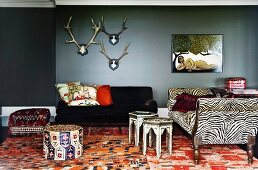 Hirschgeweihe und naive Malerei über Sitzgruppe in wildem Stilmix - antikes Sofa mit Zebramuster zu orientalischen Beistelltischen und Sitzpolstern