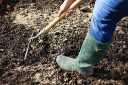 A lady wearing wellingtons mixing earth and sand together with a rake