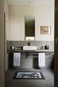 View through open door into simple bathroom with minimalist washstand counter against wall painted light grey to half height
