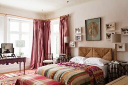 Butterfly collection on wall above wicker headboard of double bed, striped textiles and antique dressing table in front of lattice windows