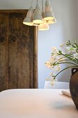 Retro style hanging lamp with porcelain shades above a dining table in front of a rustic cupboard against a wall
