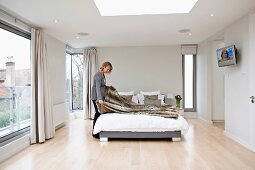 Woman making a bed in an elegant bedroom with floor to ceiling windows