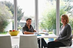Woman and man taking a coffee break at a modern dining table in front of French doors