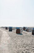 Strandkörbe neben Holzsteg am Sandstrand